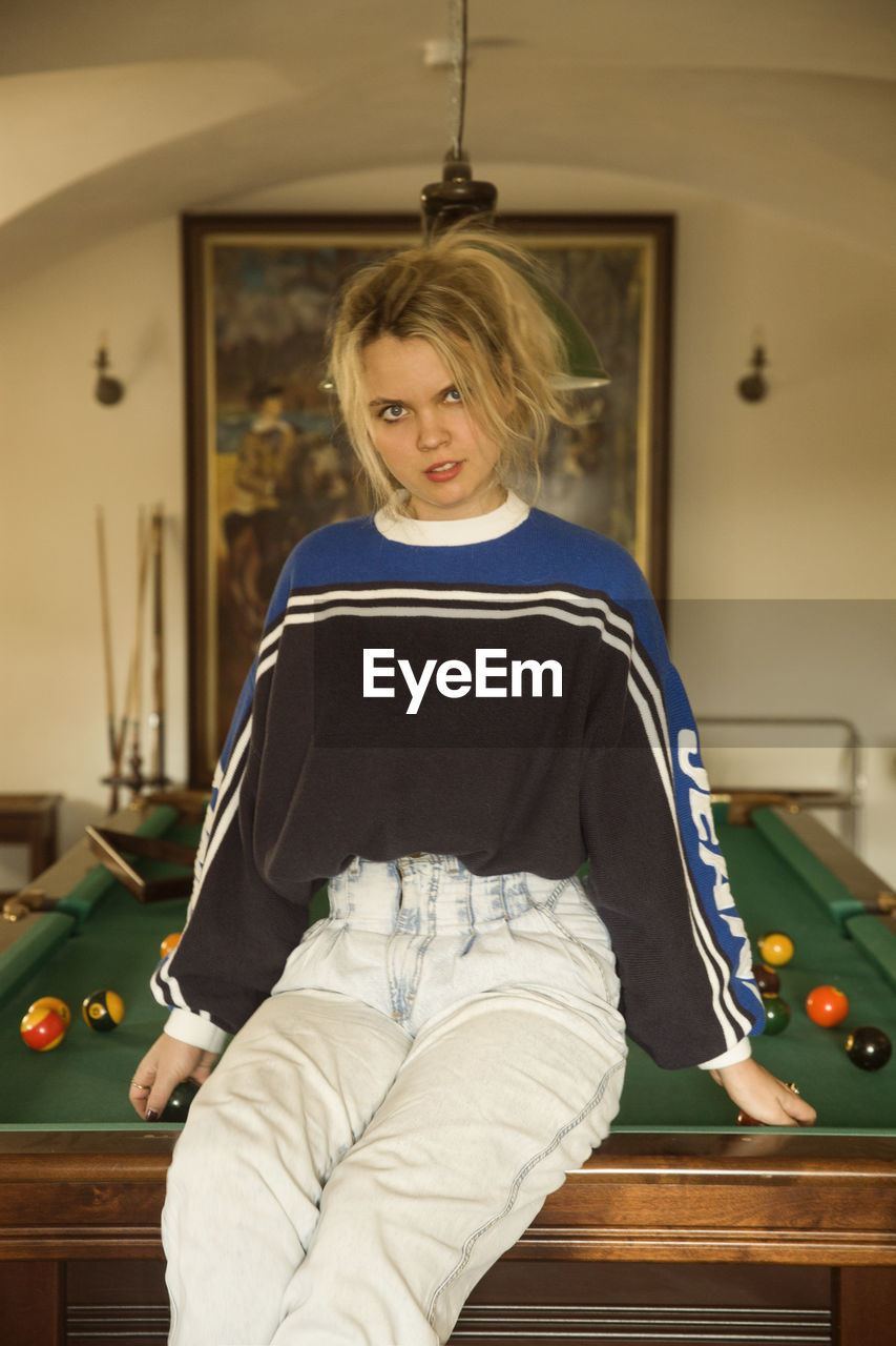 Portrait of young woman sitting on pool table