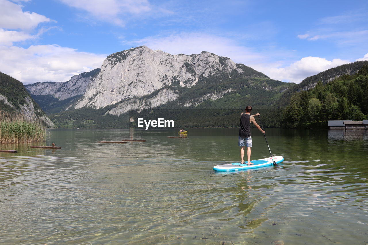 Man standing on paddleboard in lake against mountain