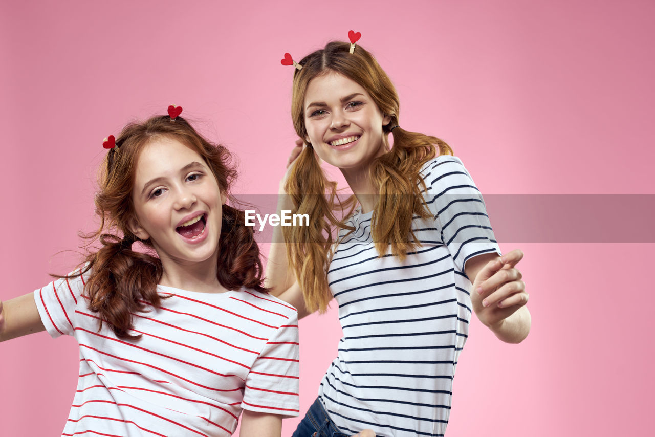 happiness, smiling, women, emotion, striped, child, fun, studio shot, colored background, portrait, togetherness, childhood, pink, positive emotion, female, indoors, two people, cheerful, looking at camera, friendship, casual clothing, adult, enjoyment, laughing, waist up, long hair, hairstyle, joy, teeth, blond hair, bonding, smile, family, clothing, carefree, person, love, front view, humor, teenager, photo shoot, young adult, facial expression, standing, pink background, lifestyles, brown hair