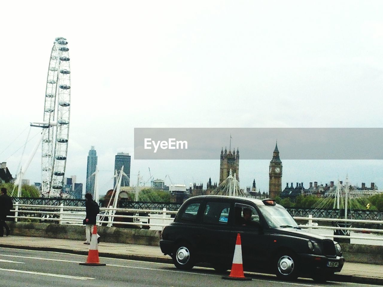 Black car on bridge in front of millennium wheel and big ben against sky in city