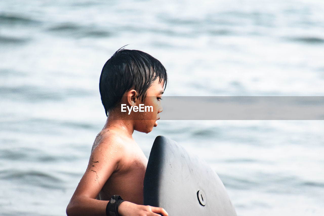 Shirtless boy with surfboard on beach