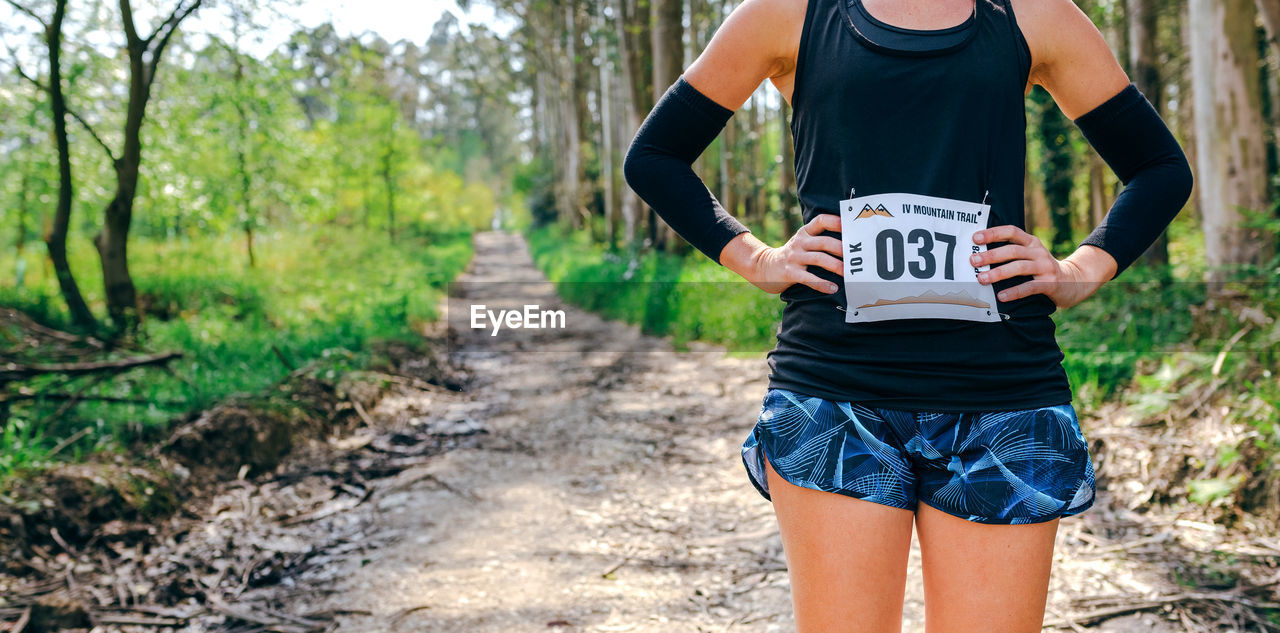 Midsection of woman standing with marathon bib in forest
