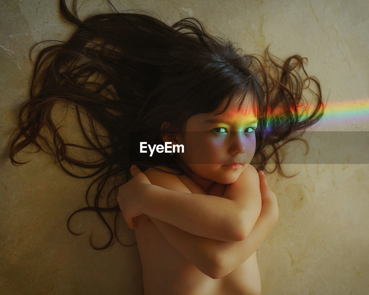 Close-up of young girl laying on the floor with rainbow light falling on her face