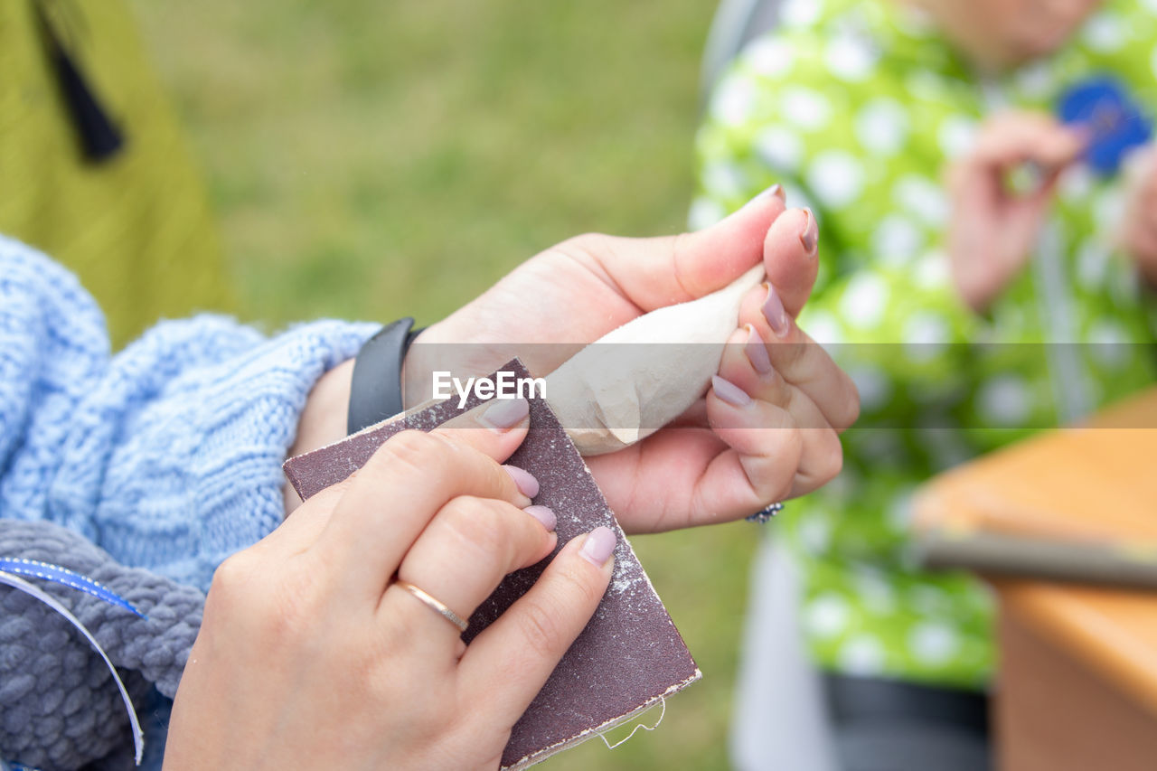 CLOSE-UP OF WOMAN HOLDING HANDS AGAINST BLURRED OUTDOORS