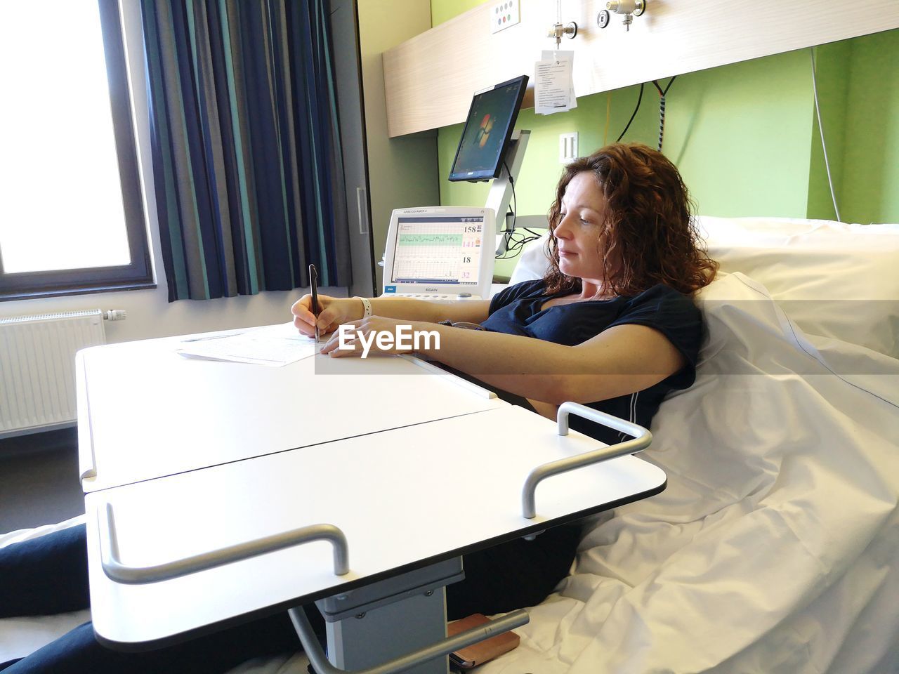 Woman writing while sitting on bed at hospital