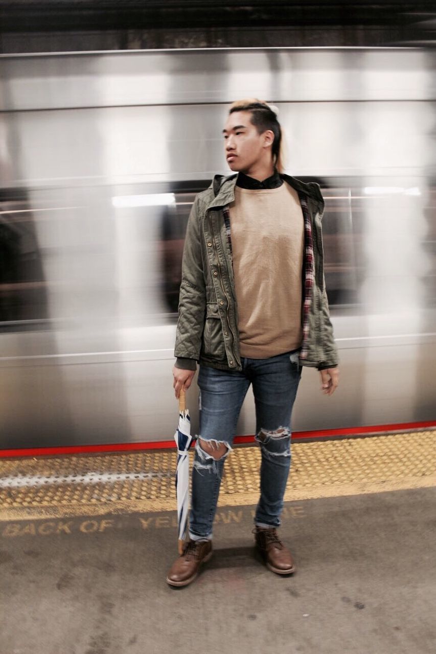 Full length of man holding umbrella while standing by moving train at railroad station