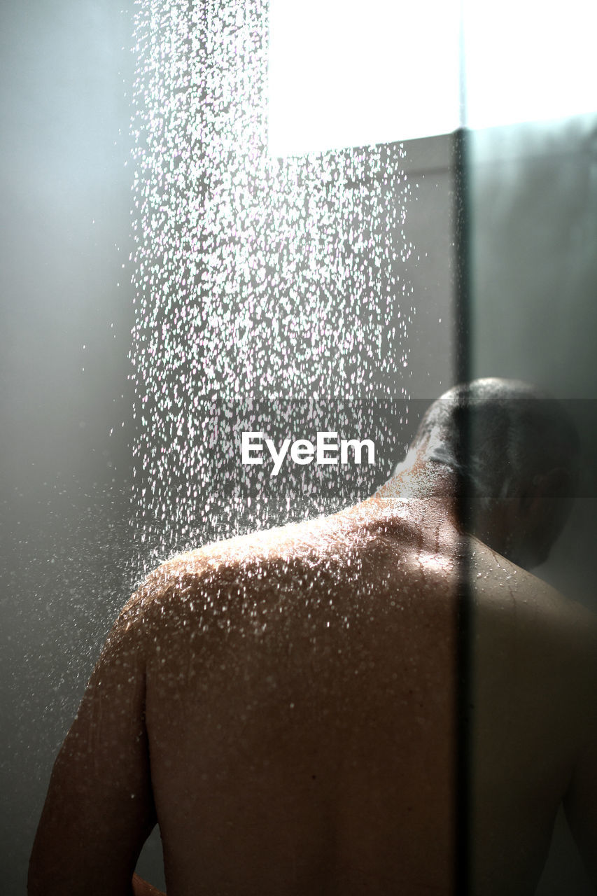 Rear view of man taking shower in bathroom