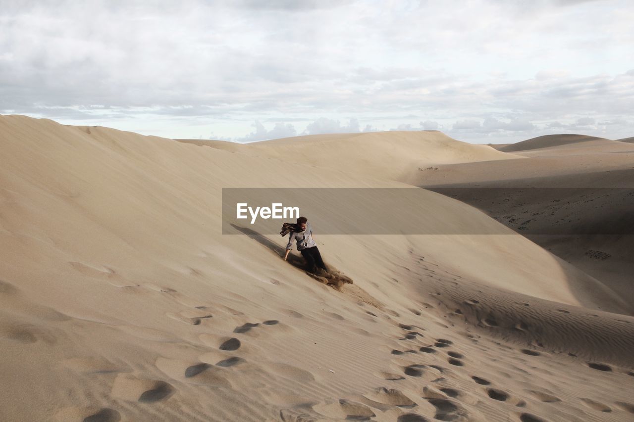 Man on sand dune at desert against sky