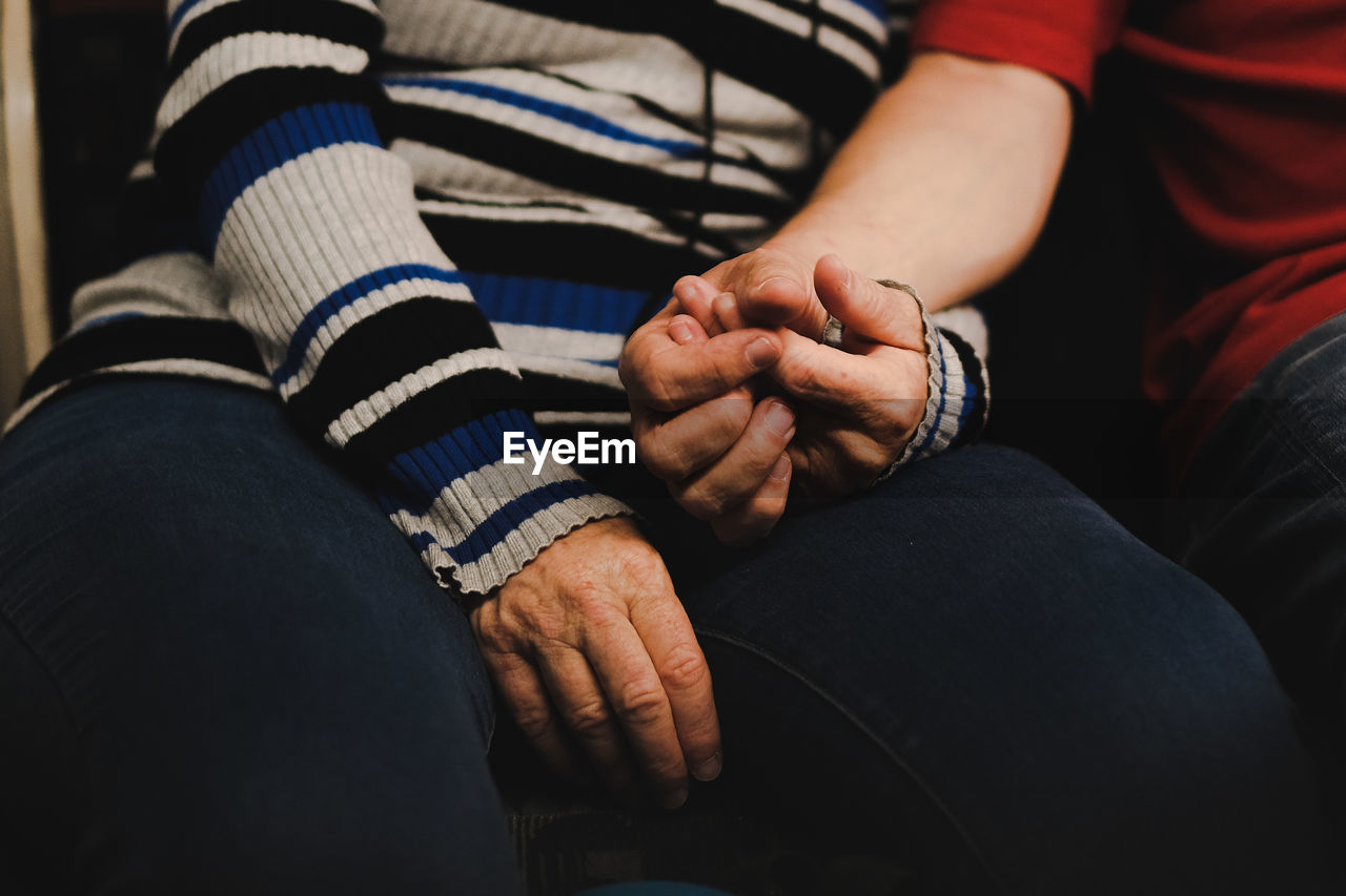 Midsection of man and woman holding hand sitting at home
