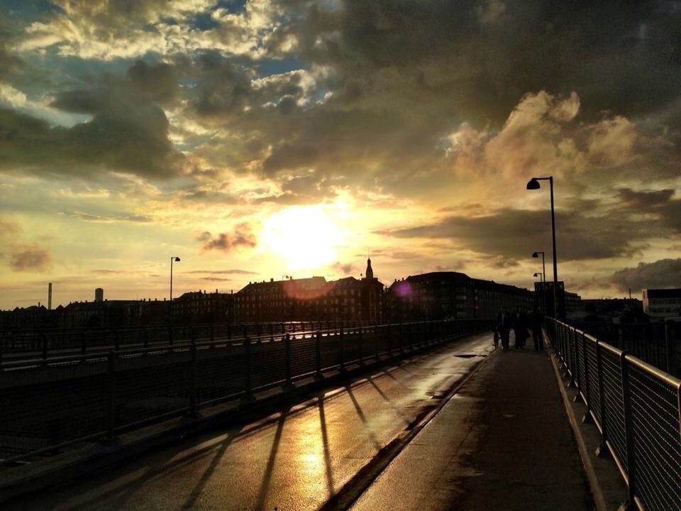 Walkway bridge by city against bright sky