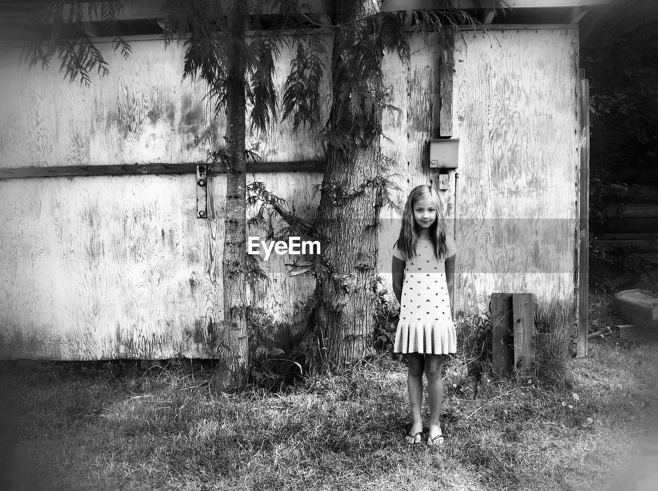 Full length portrait of girl standing on grass against wooden wall