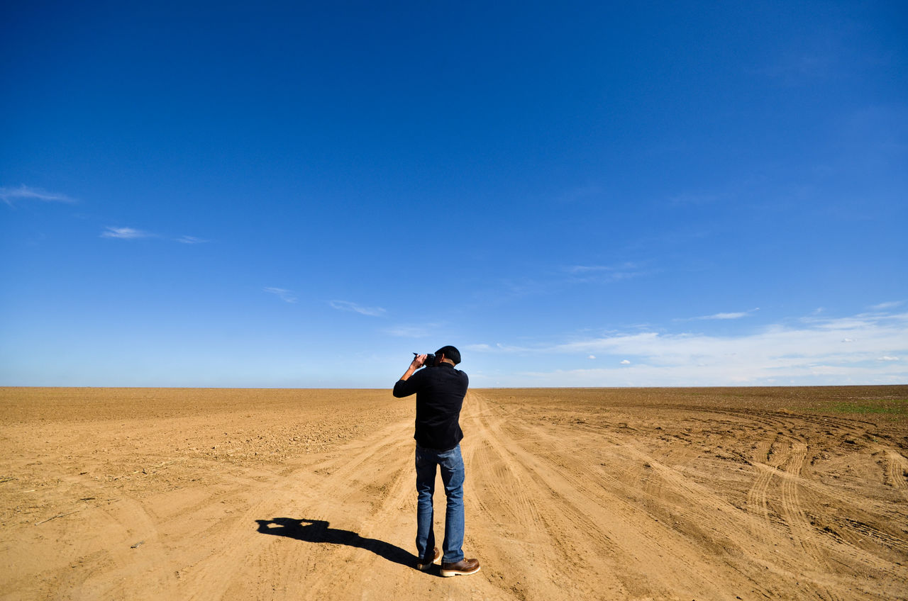 Rear view of man photographing on landscape against blue sky