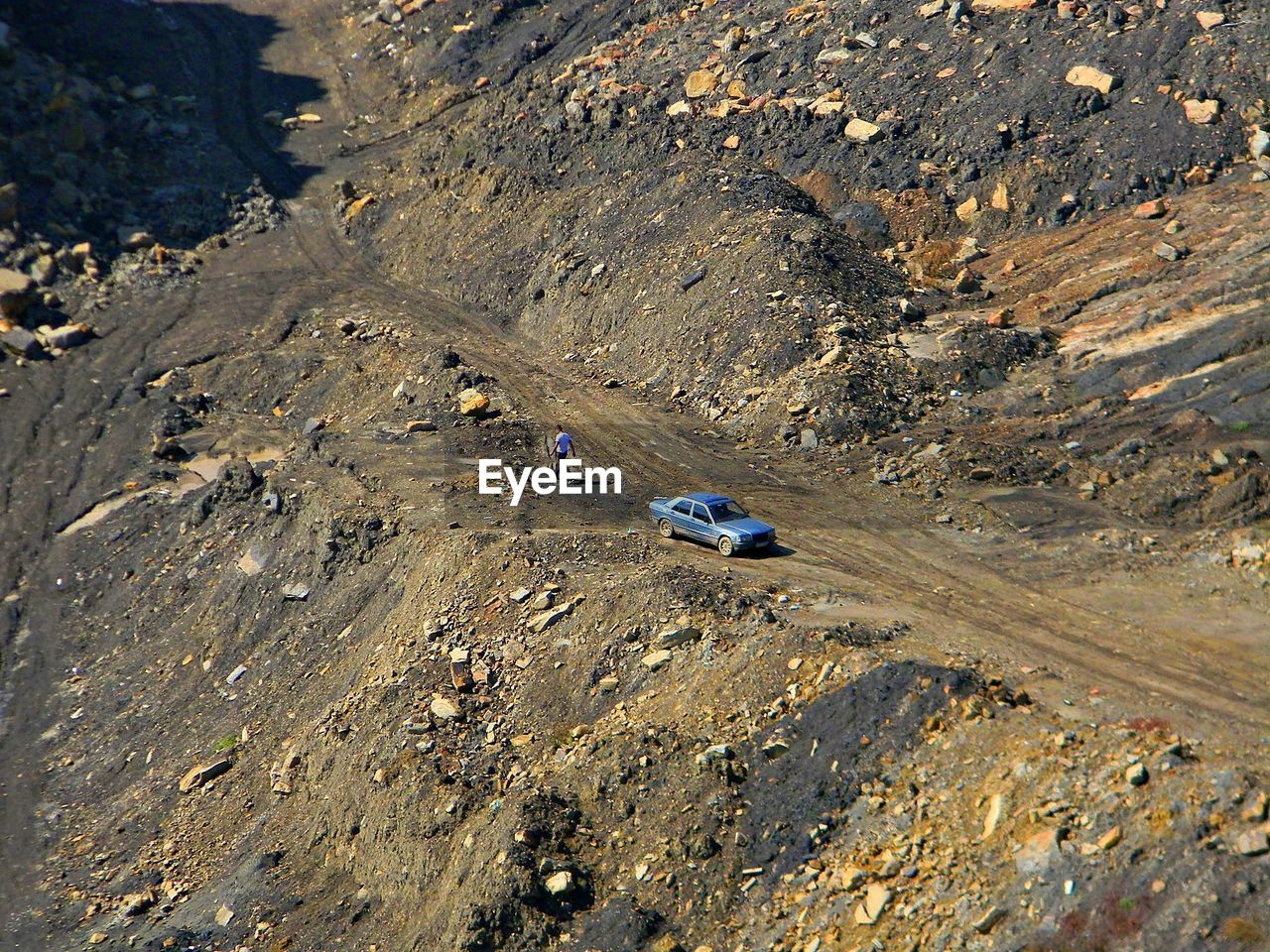 High angle view of man by car on dirt road on mountain