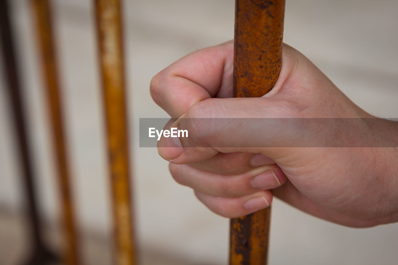 Close-up of man holding rusty prison bars