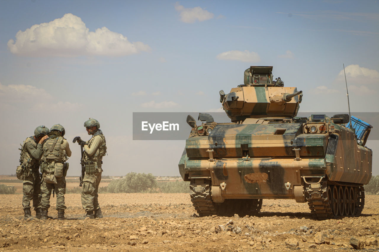 Soldiers discussing while standing by armor tank against sky