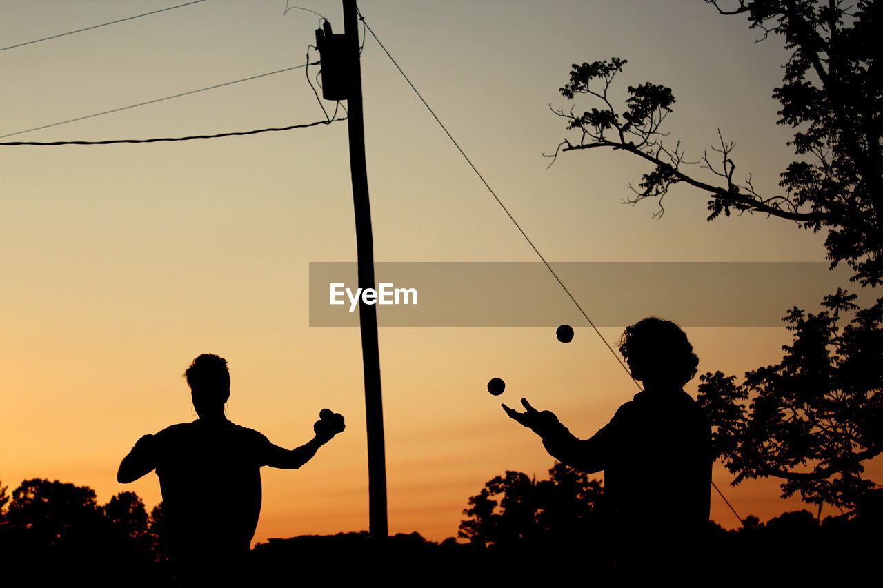 Silhouette people juggling balls against sky during sunset