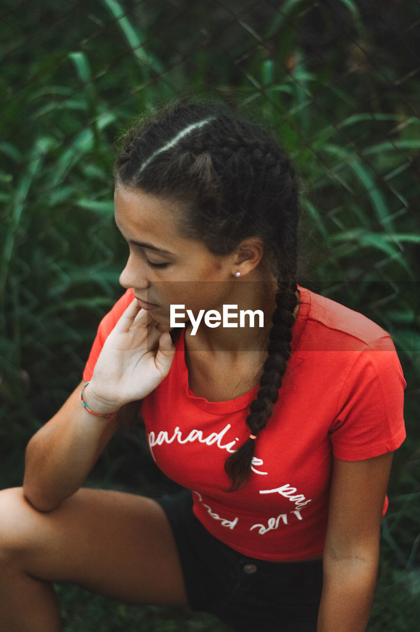YOUNG WOMAN LOOKING DOWN WHILE SITTING ON LAND