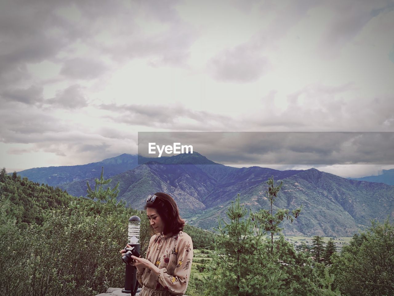 Woman using camera while standing against mountains