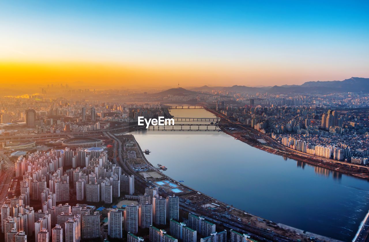 Aerial view of river amidst buildings in city during sunrise