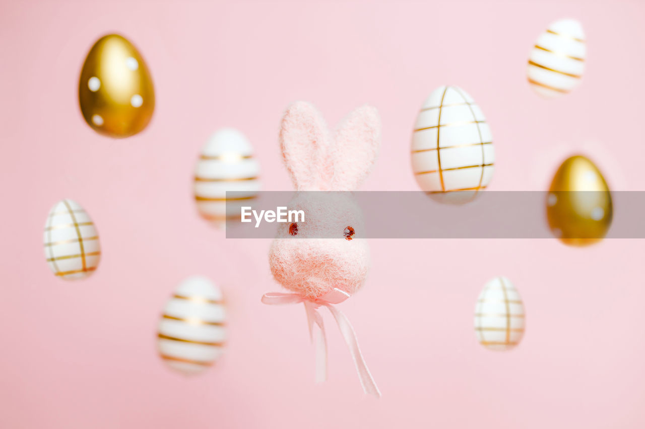 Easter bunny and golden eggs levitating against pink background. fluffy rabbit with tie. 