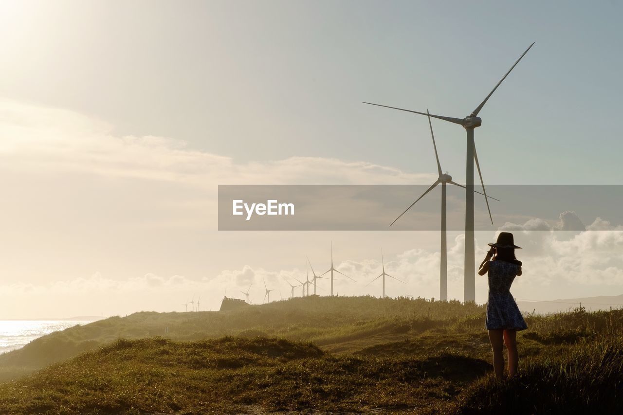 Woman standing on field with wind turbines against sky