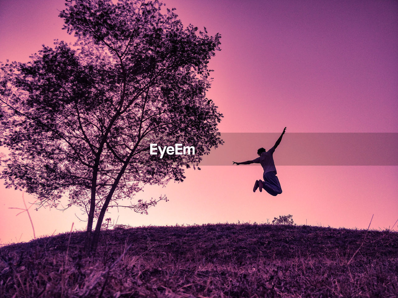 Low angle view of man jumping on field against sky during sunset