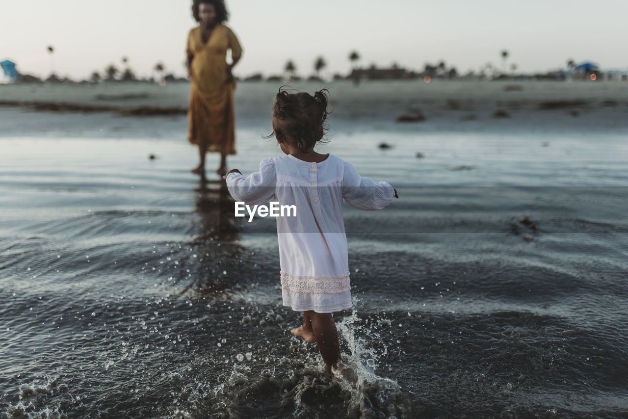 Young toddler girl splashing in the sea with family negative space