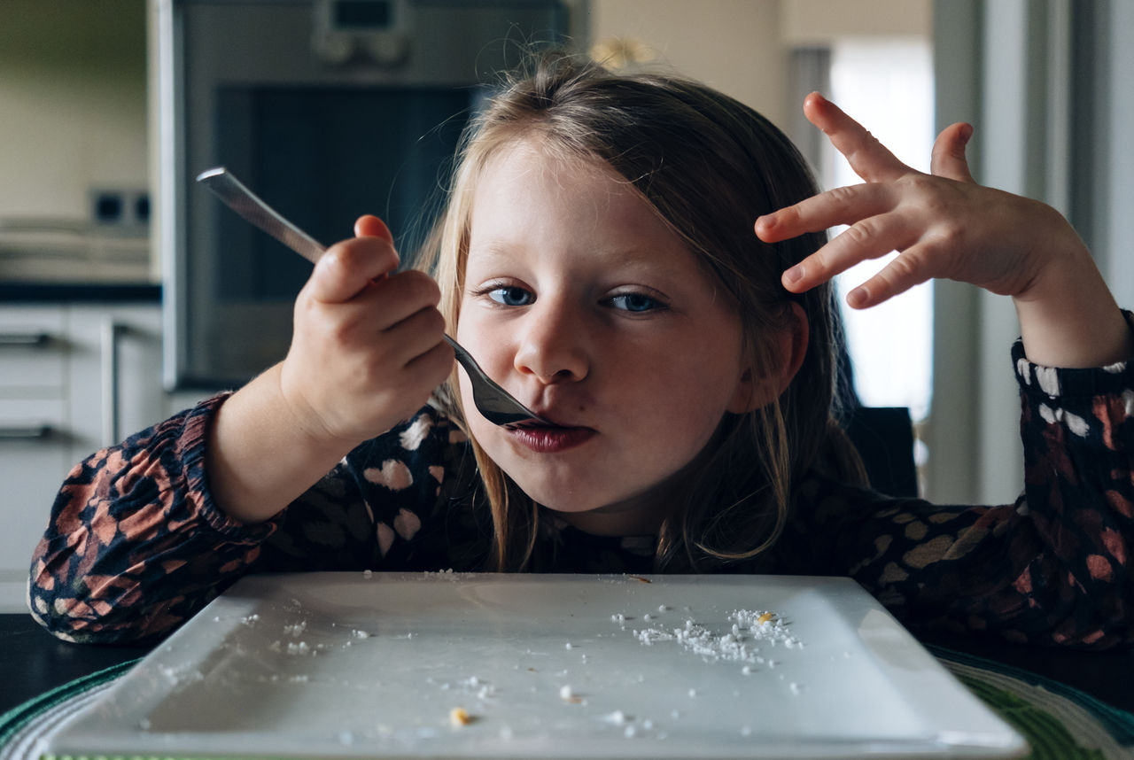 Portrait of girl eating food in plate at home