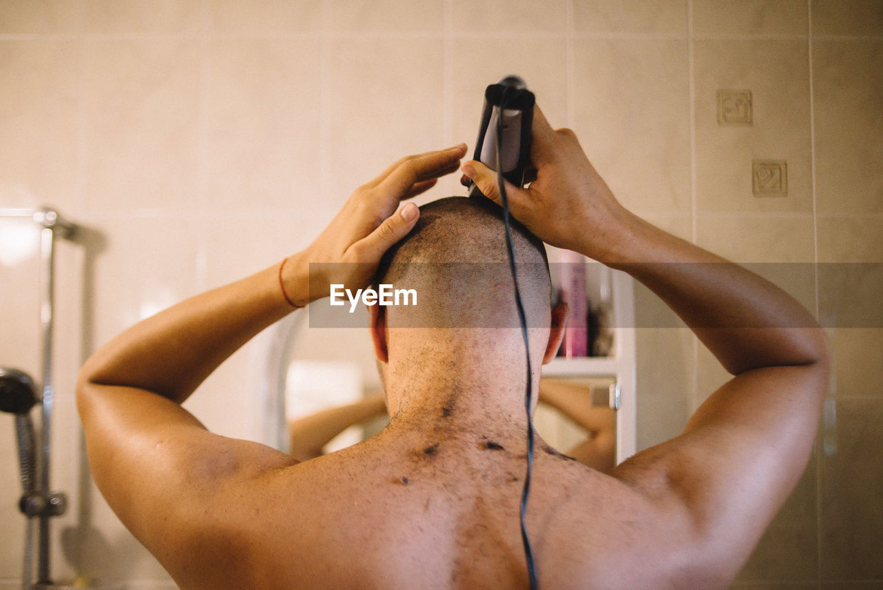 Rear view of man shaving head in bathroom