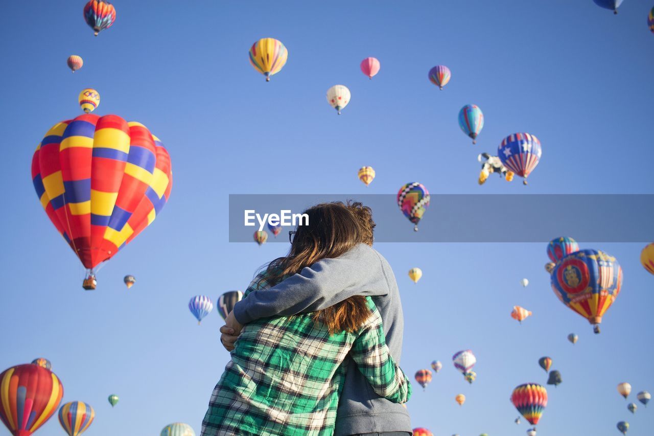 Low angle view of couple embracing against hot air balloons flying in sky