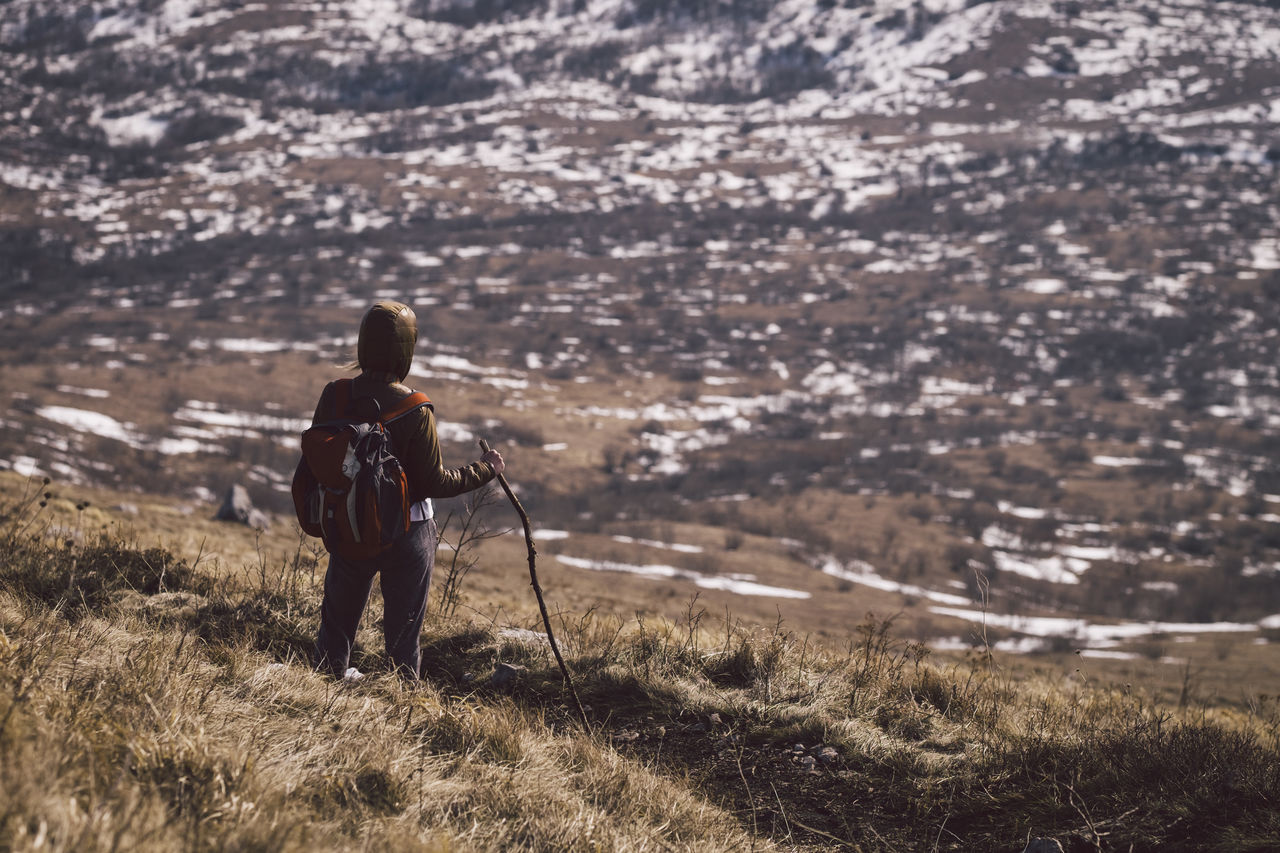 Rear view of backpack hiker standing on mountain against landscape during winter