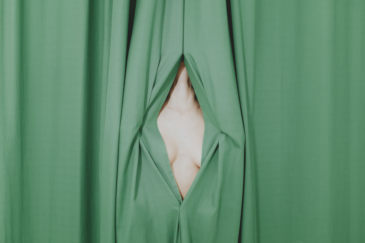 Midsection of naked woman hiding behind curtain