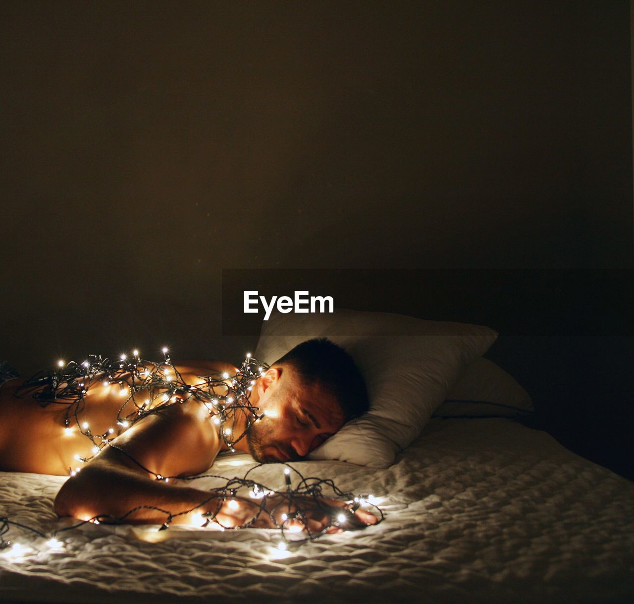 Man sleeping with illuminated string lights on bed at home