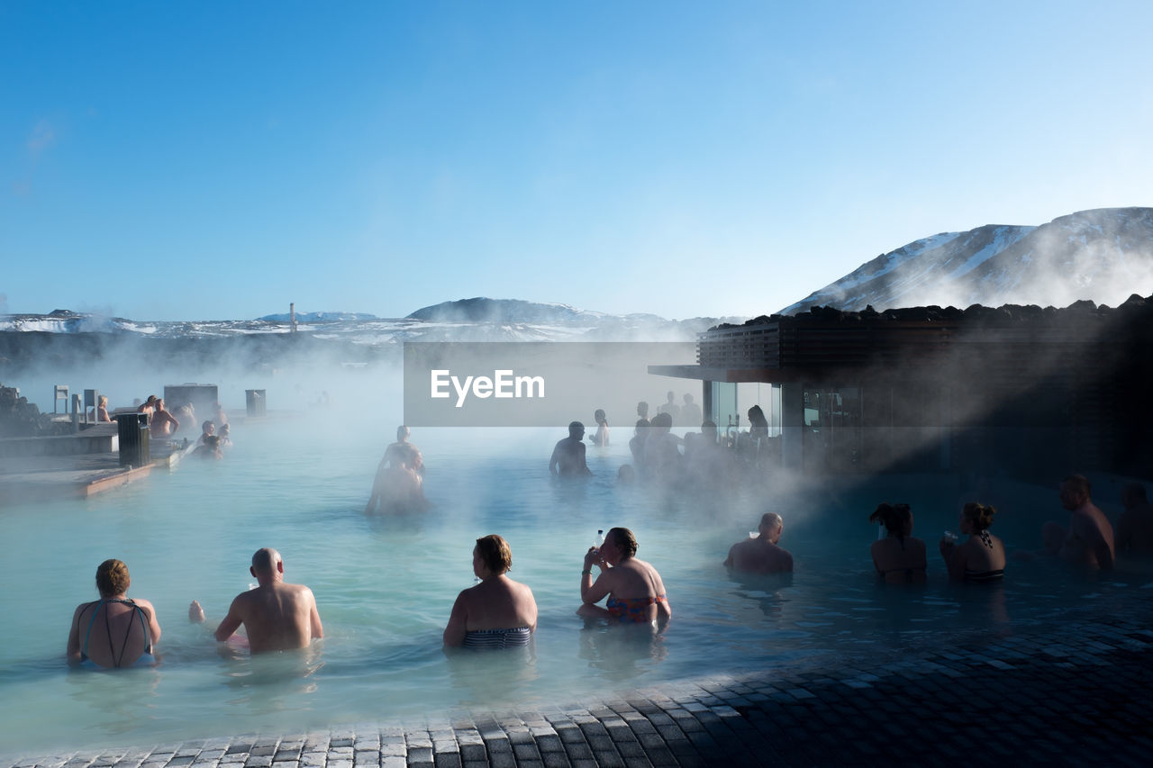People resting in hot spring against clear blue sky