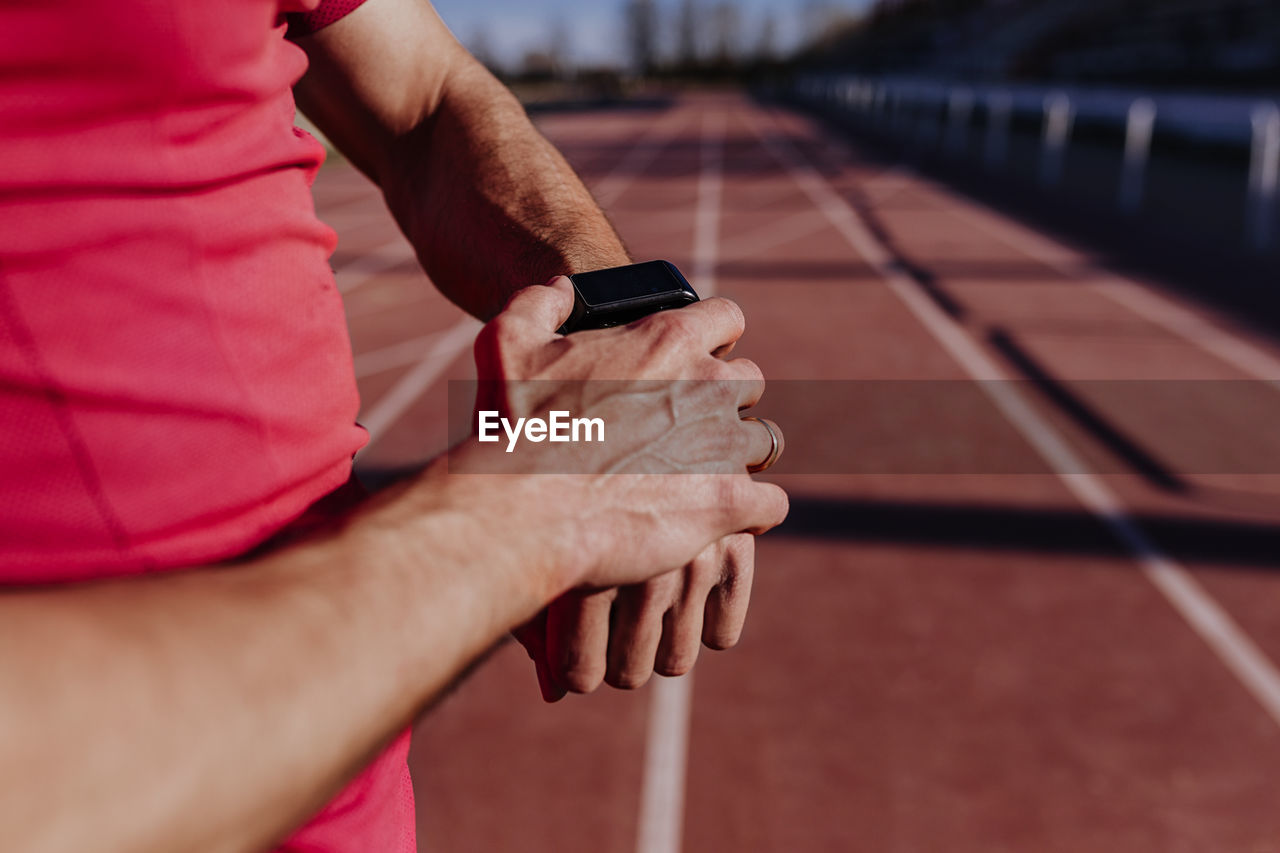 Midsection of athlete wearing smart watch on sports track