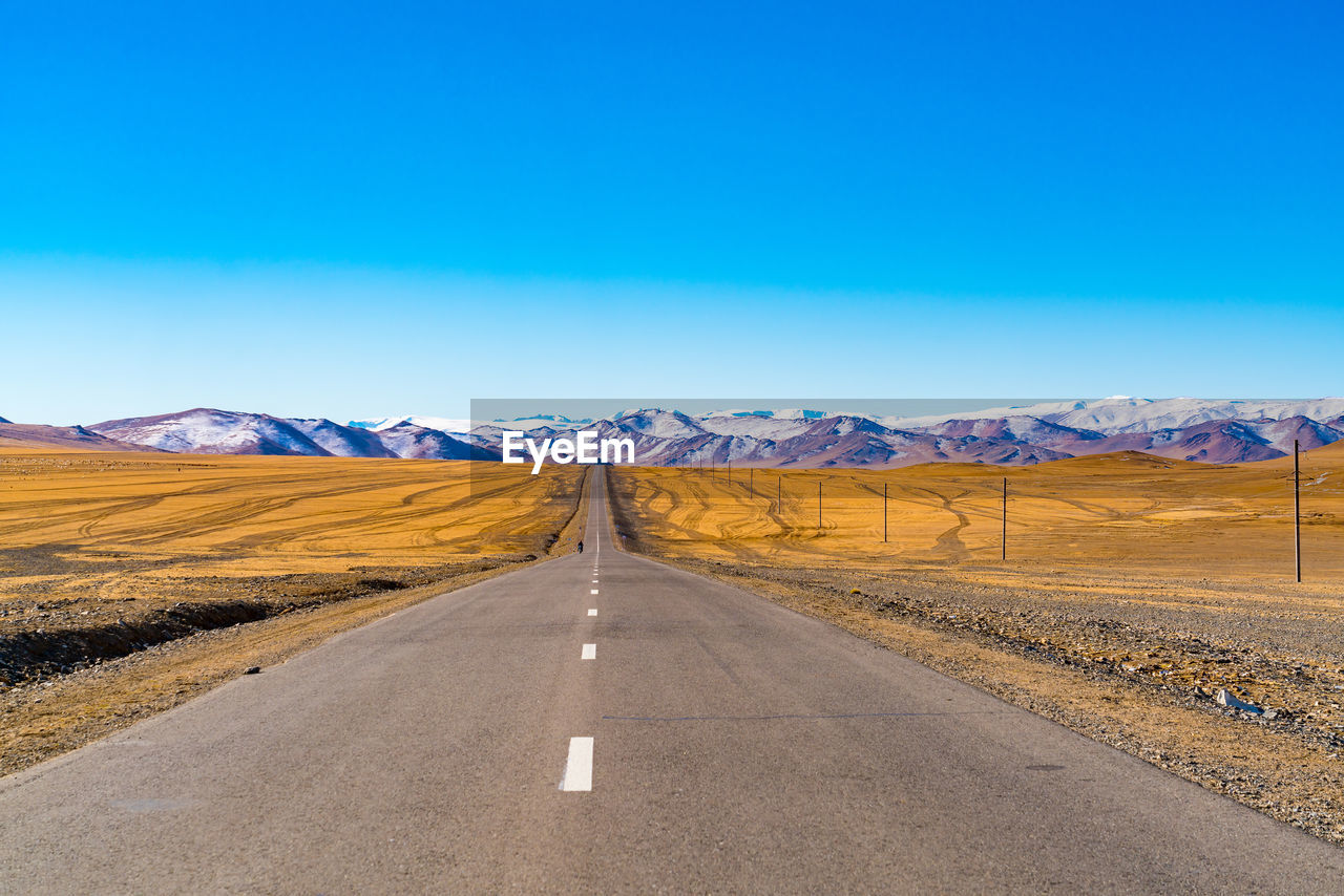 Road leading towards snowcapped mountains against blue sky