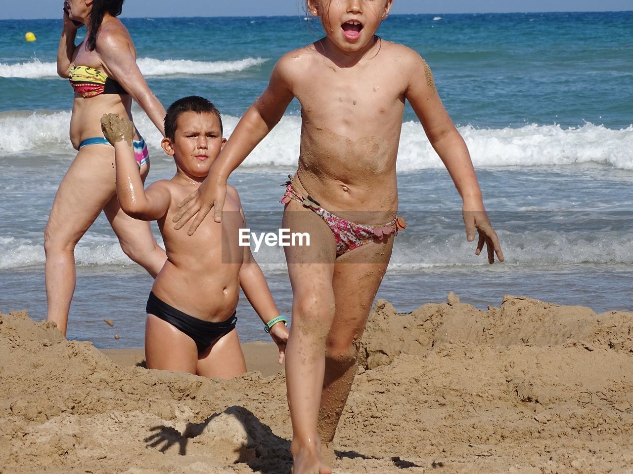 Shirtless siblings playing with sand at beach