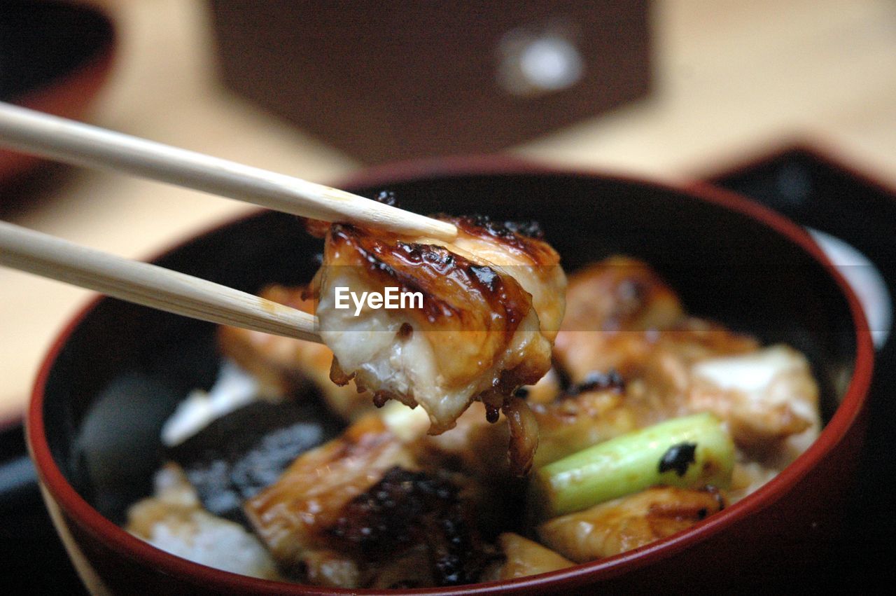 Close-up of chopsticks holding unagi  in bowl