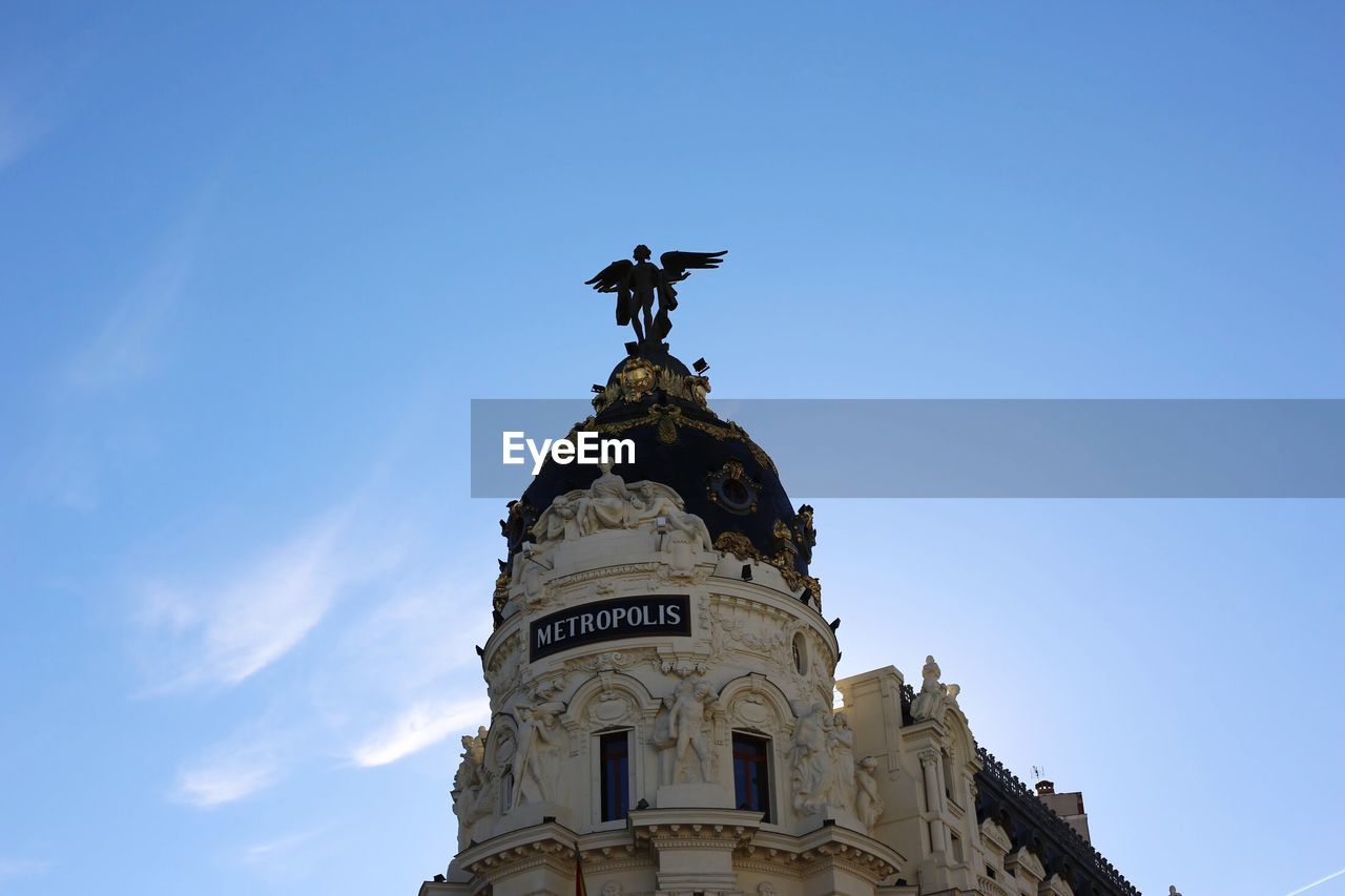 Low angle view of statue on building against blue sky