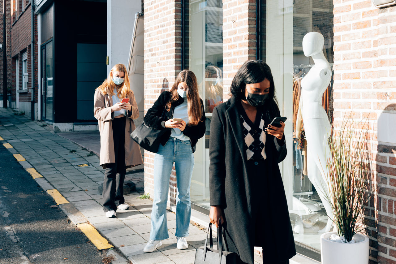 Girls wearing face mask using a mobile phone while waiting on the street the opening of retail