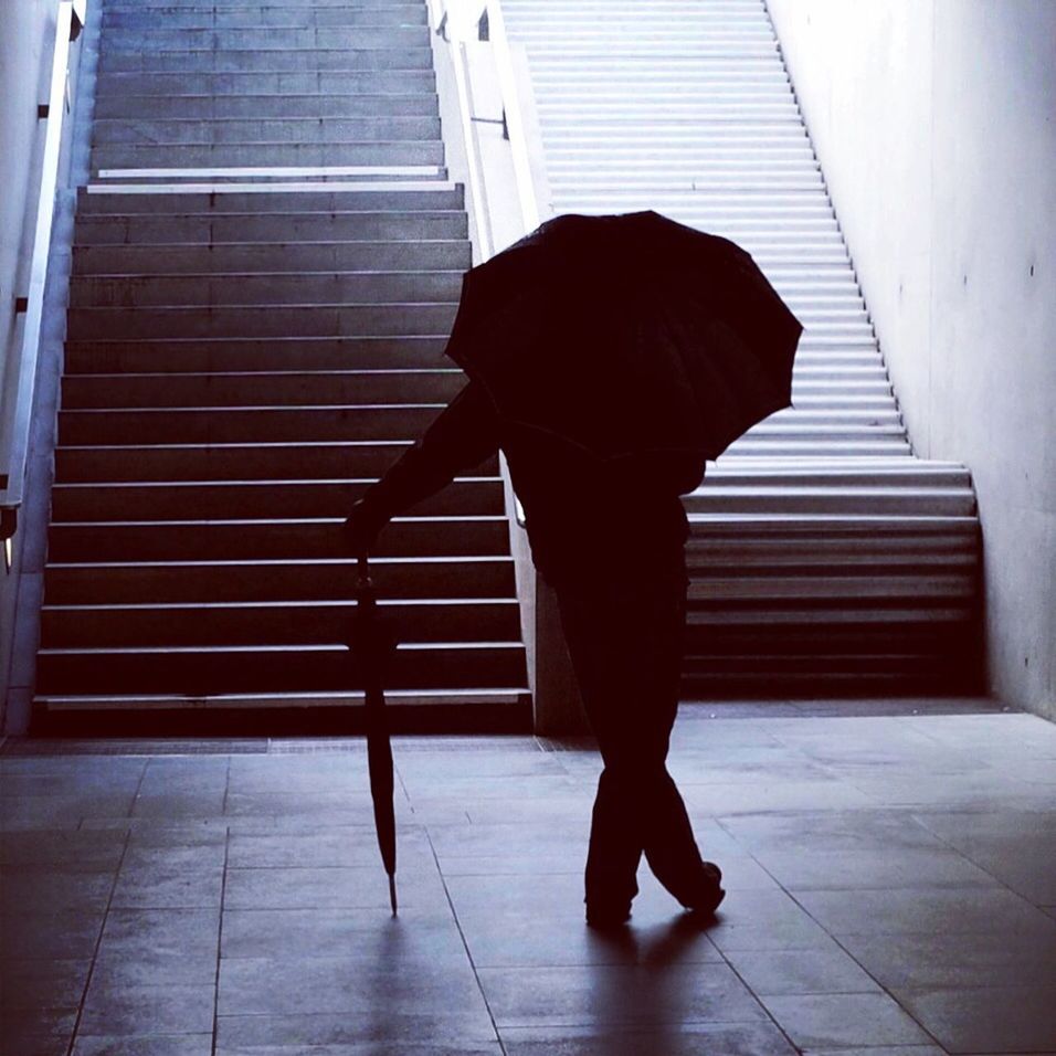 Rear view of silhouette man with umbrellas standing on underground walkway
