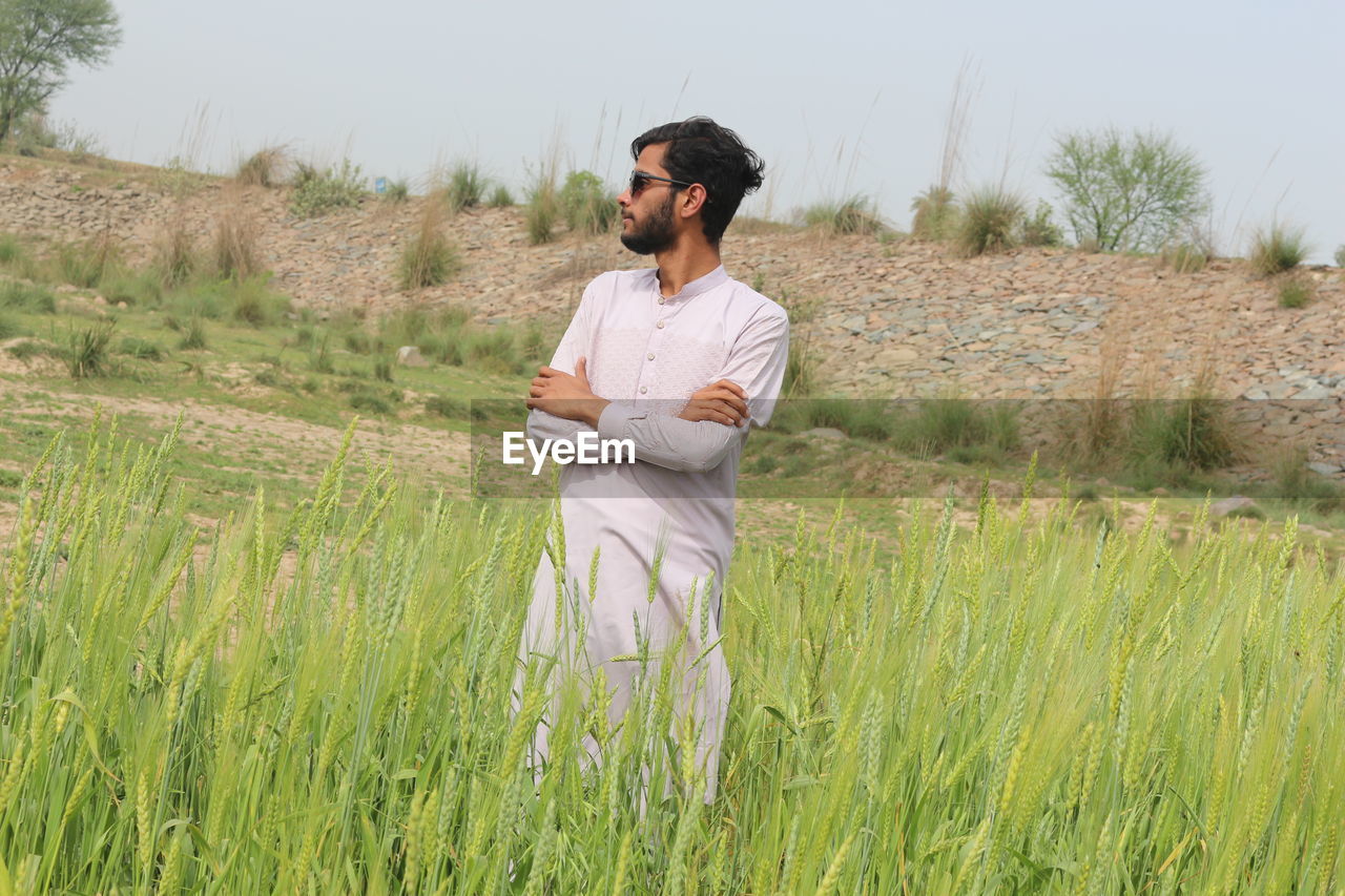 plant, one person, adult, agriculture, field, nature, land, prairie, landscape, grass, grassland, growth, rural scene, men, crop, meadow, environment, occupation, standing, young adult, rural area, casual clothing, three quarter length, sky, natural environment, looking, day, outdoors, beauty in nature, tranquility, cereal plant, paddy field, beard, facial hair, leisure activity, lifestyles, green, clothing, contemplation, scenics - nature, holding, front view, tranquil scene, non-urban scene