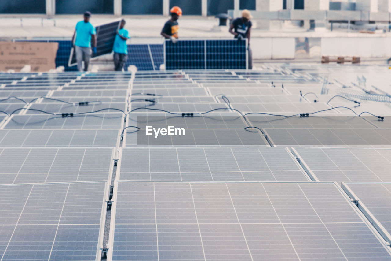 Contemporary solar panels installed in rows in industrial area of factory on background of unrecognizable ethnic workers