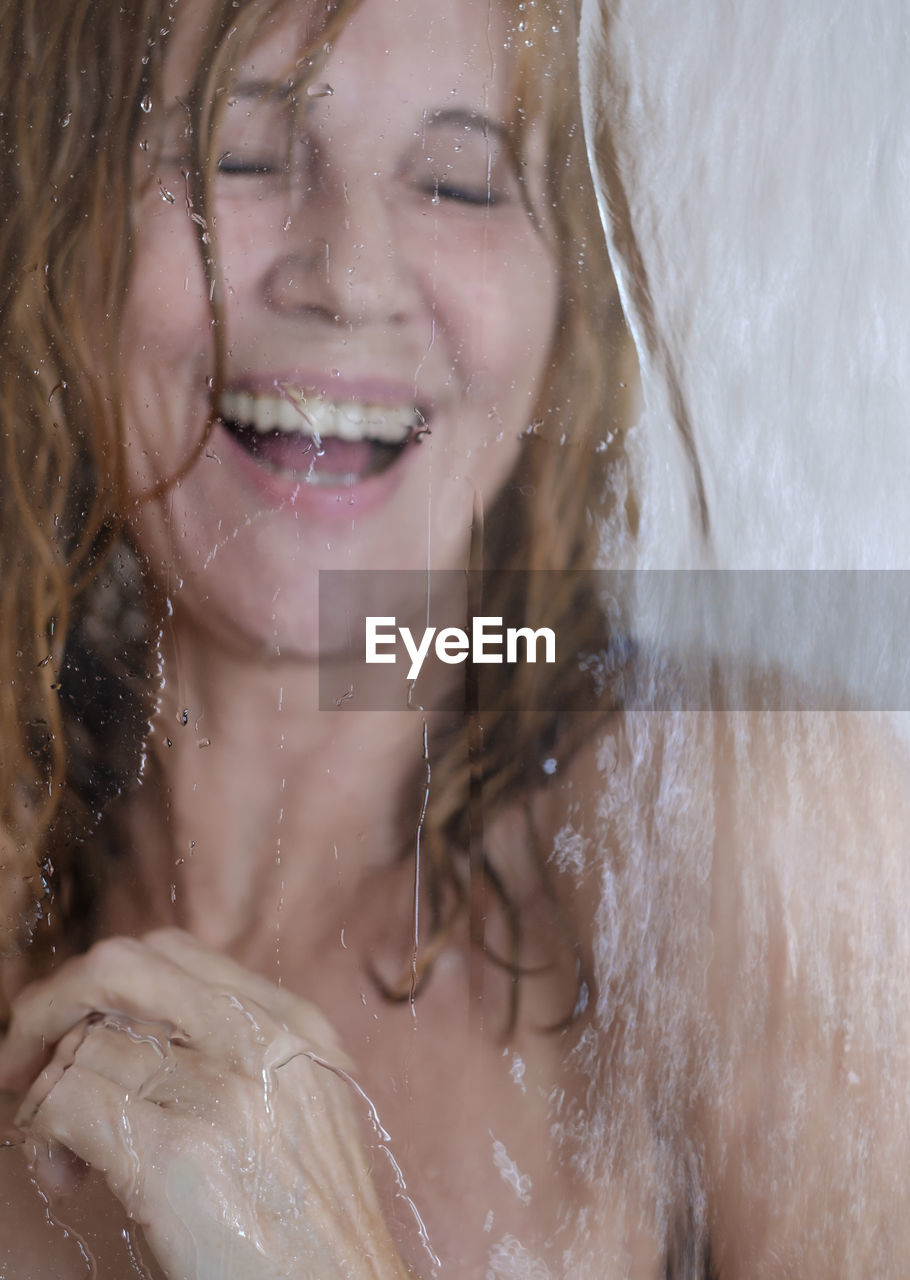 Cheerful woman in shower seen through glass