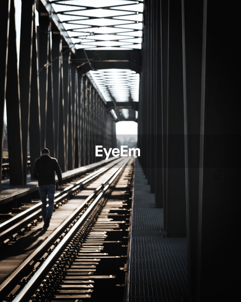 Rear view of man walking on railroad tracks
