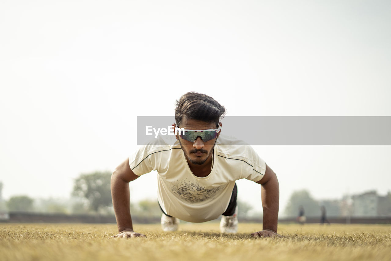 portrait of young man wearing sunglasses while standing on field against clear sky
