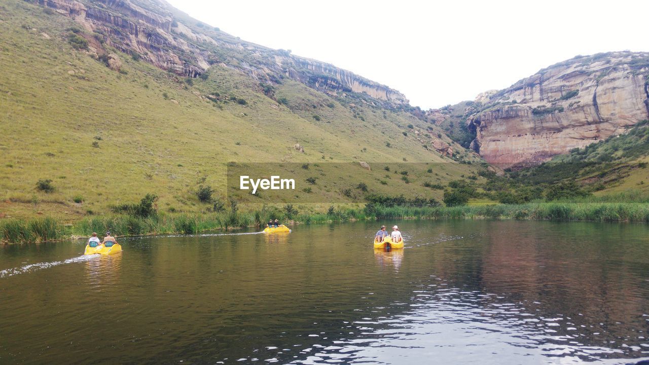 People boating in lake against mountains