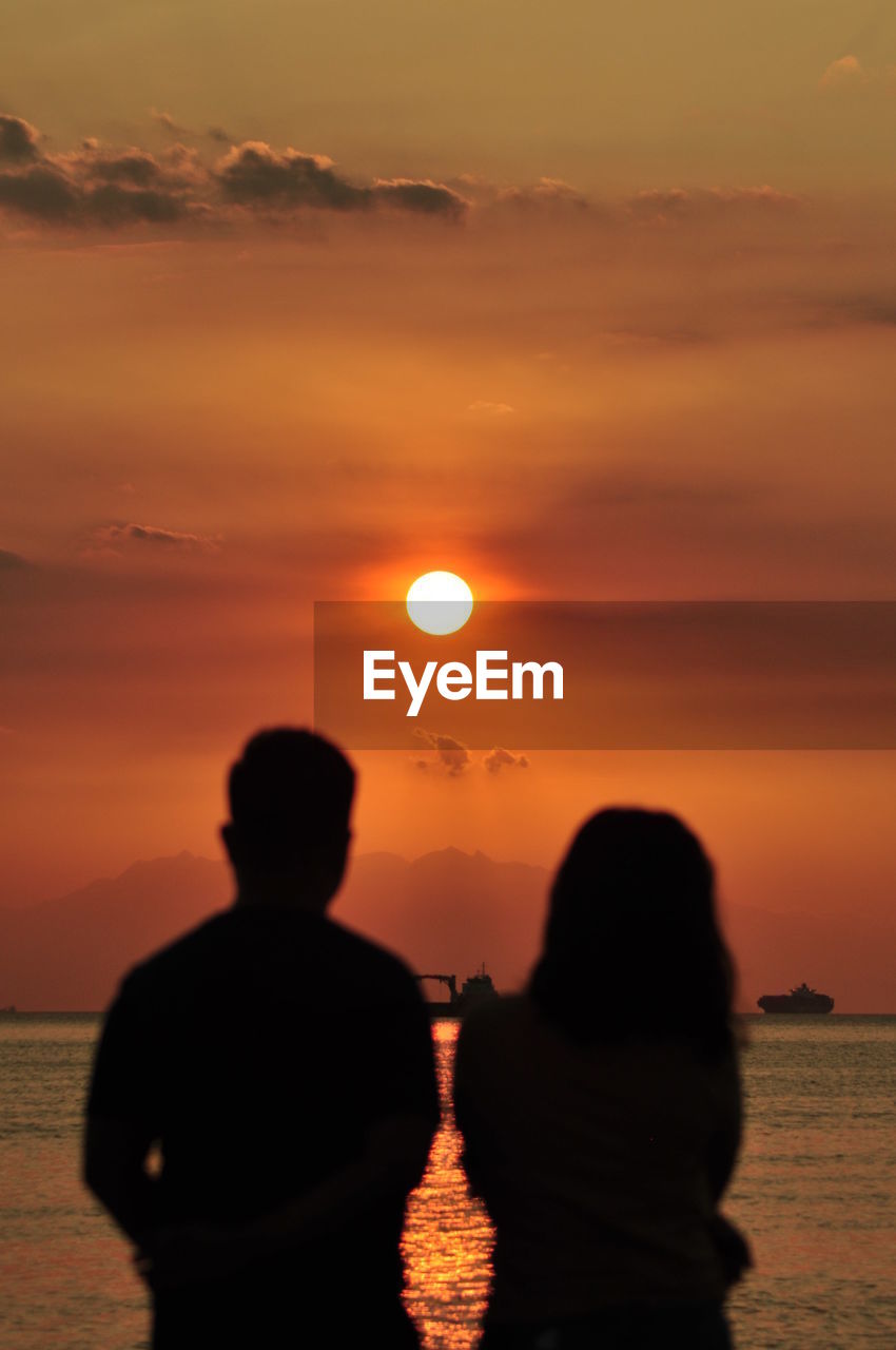 Silhouette people by sea against sky during sunset