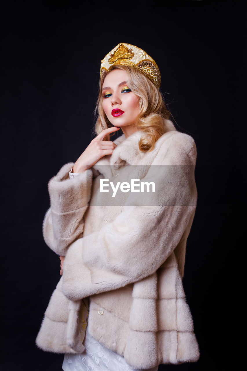 Beautiful woman wearing fur jacket and crown against black background