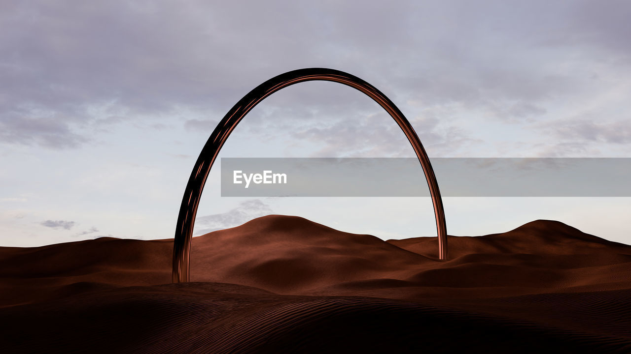 Desert dune landscape at sunset with a metal bow shaped monolith